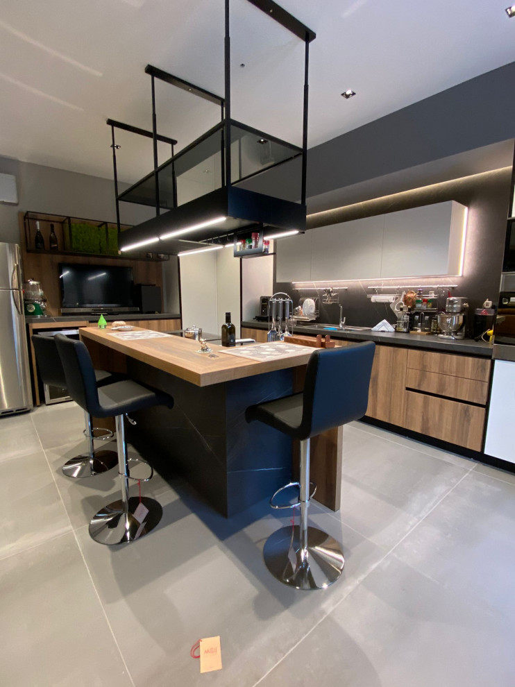Large modern l-shaped eat-in kitchen in Naples with a single-bowl sink, flat-panel cabinets, light wood cabinets, marble benchtops, black splashback, porcelain splashback, black appliances, porcelain floors, with island, grey floor, grey benchtop and recessed.
