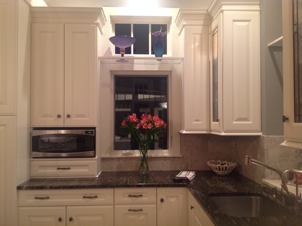Inspiration for a mid-sized transitional u-shaped travertine floor eat-in kitchen remodel in New York with an undermount sink, raised-panel cabinets, white cabinets, granite countertops, beige backsplash, stone tile backsplash, stainless steel appliances and an island