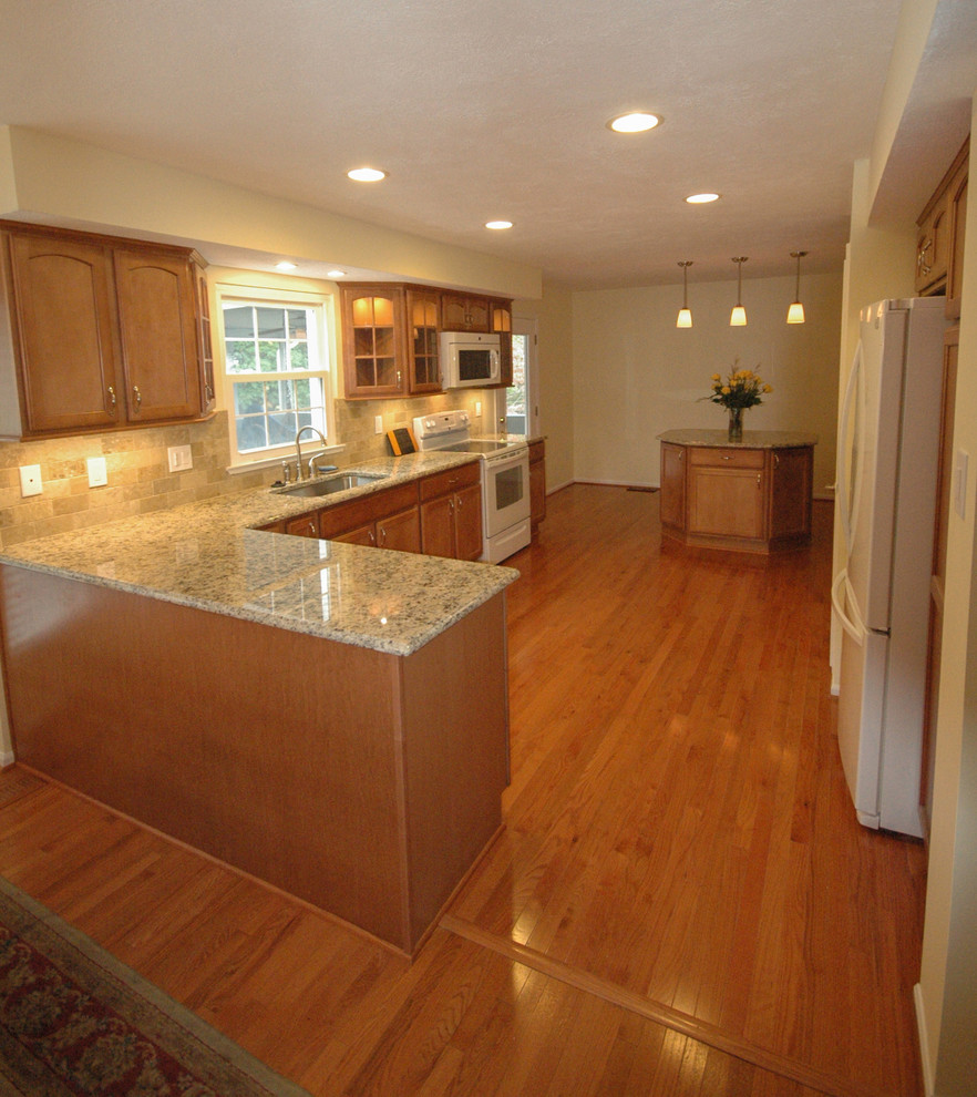 Photo of a mid-sized traditional l-shaped separate kitchen in Baltimore with an undermount sink, recessed-panel cabinets, medium wood cabinets, granite benchtops, beige splashback, white appliances, medium hardwood floors and no island.
