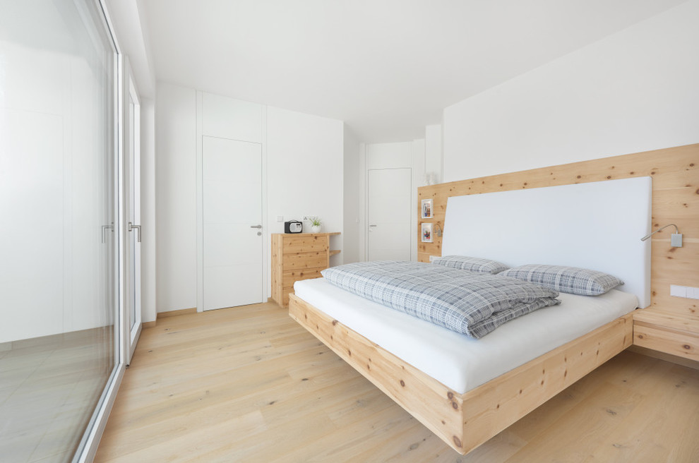 Mid-sized scandinavian master bedroom in Other with white walls and light hardwood floors.