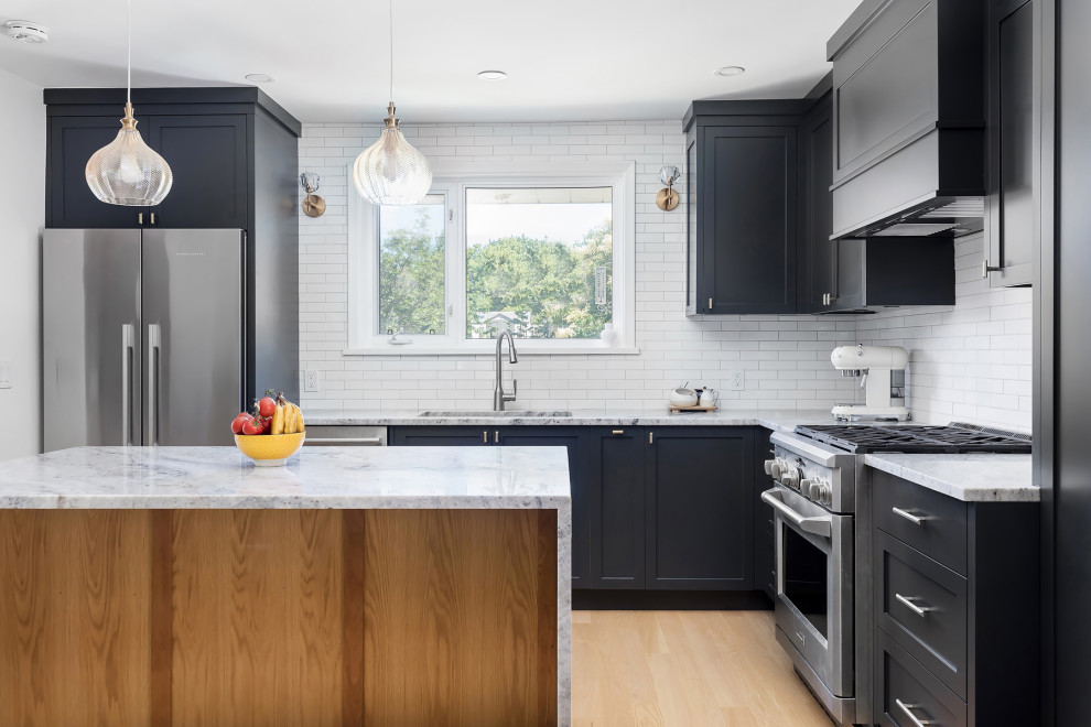 Inspiration for a mid-sized transitional l-shaped open plan kitchen in Toronto with an undermount sink, shaker cabinets, black cabinets, granite benchtops, white splashback, ceramic splashback, stainless steel appliances, light hardwood floors, with island, brown floor, grey benchtop and wallpaper.