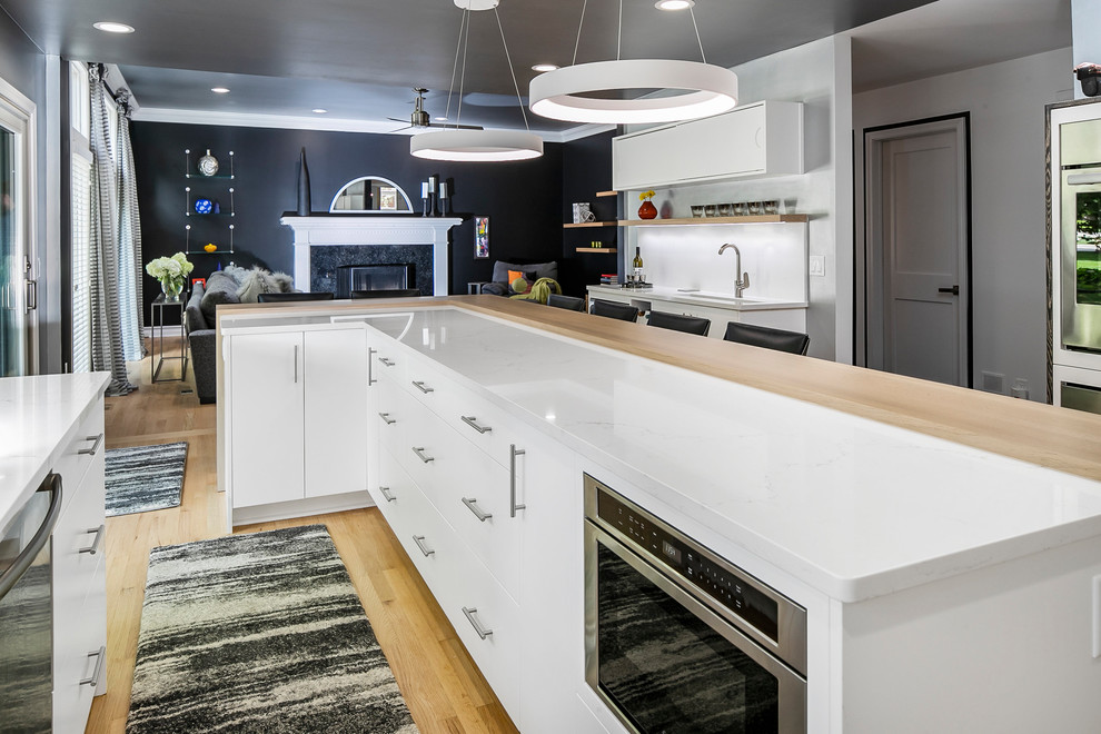Photo of a large contemporary l-shaped eat-in kitchen in Detroit with an undermount sink, flat-panel cabinets, white cabinets, quartz benchtops, white splashback, stone slab splashback, stainless steel appliances, medium hardwood floors, with island, brown floor and white benchtop.