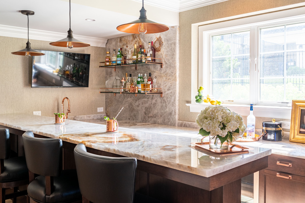 Photo of a large transitional u-shaped wet bar in Philadelphia with a drop-in sink, beaded inset cabinets, brown cabinets, quartzite benchtops, beige splashback, stone slab splashback, ceramic floors, brown floor and white benchtop.