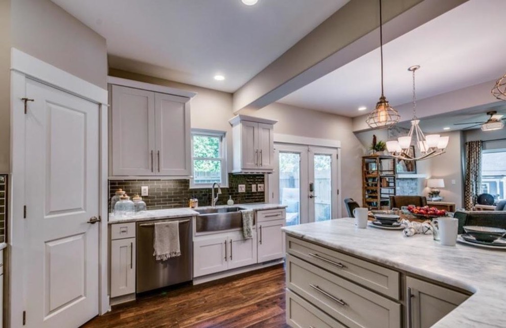 This is an example of a mid-sized transitional eat-in kitchen in Orange County with a farmhouse sink, shaker cabinets, white cabinets, marble benchtops, brown splashback, ceramic splashback, stainless steel appliances, dark hardwood floors and a peninsula.