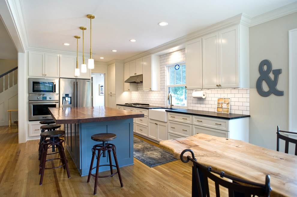 Inspiration for a mid-sized transitional l-shaped light wood floor and brown floor eat-in kitchen remodel with a farmhouse sink, raised-panel cabinets, white cabinets, quartz countertops, white backsplash, subway tile backsplash, stainless steel appliances and an island