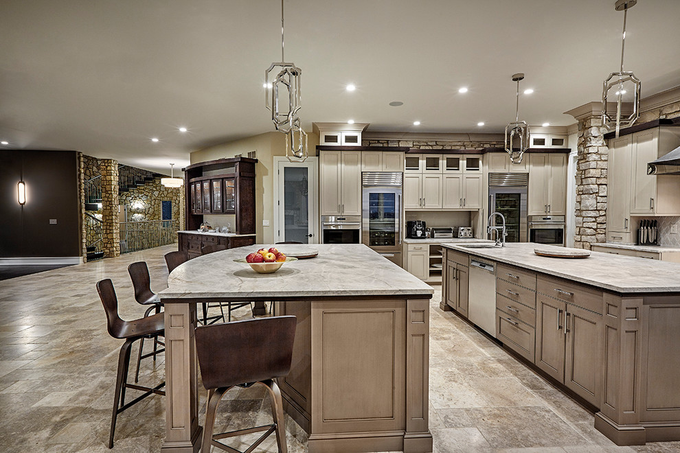 This is an example of an expansive transitional u-shaped eat-in kitchen in Chicago with an undermount sink, recessed-panel cabinets, beige cabinets, quartzite benchtops, white splashback, stone tile splashback, stainless steel appliances, limestone floors and multiple islands.