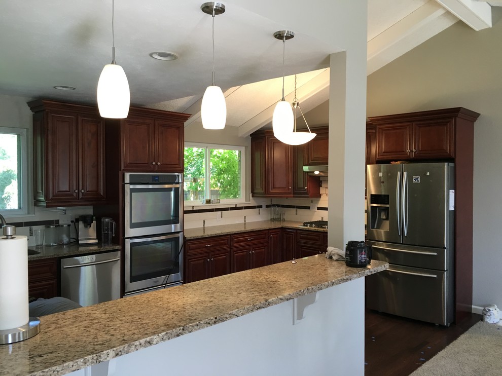 Inspiration for a mid-sized transitional l-shaped laminate floor and brown floor open concept kitchen remodel in Denver with an undermount sink, raised-panel cabinets, dark wood cabinets, granite countertops, multicolored backsplash, ceramic backsplash, stainless steel appliances and an island