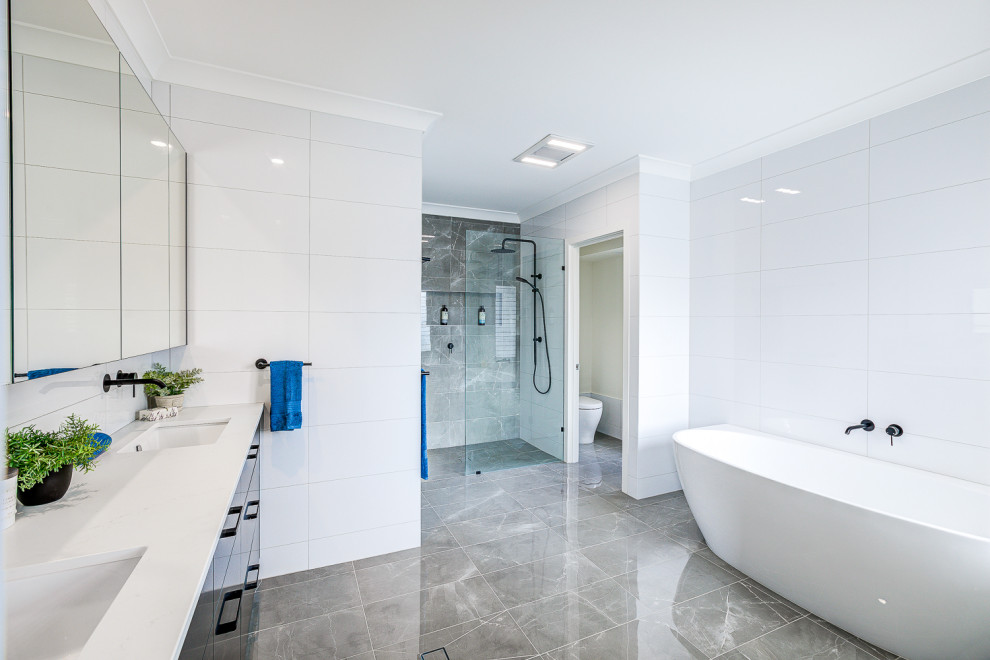 Inspiration for an expansive contemporary master bathroom in Brisbane with shaker cabinets, black cabinets, a freestanding tub, an open shower, a one-piece toilet, white tile, ceramic tile, ceramic floors, engineered quartz benchtops, brown floor, an open shower, white benchtops, an enclosed toilet, a double vanity and a built-in vanity.