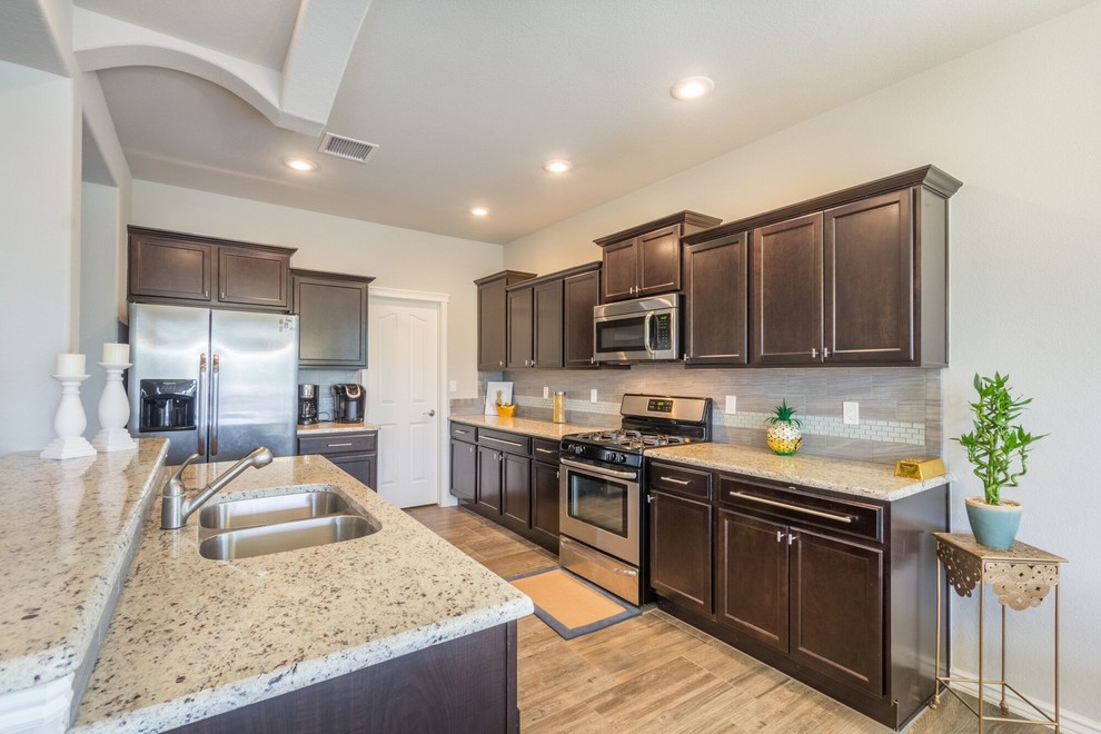 Inspiration for a mid-sized transitional u-shaped ceramic tile eat-in kitchen remodel in Austin with a double-bowl sink, raised-panel cabinets, dark wood cabinets, granite countertops, gray backsplash, ceramic backsplash, stainless steel appliances and an island