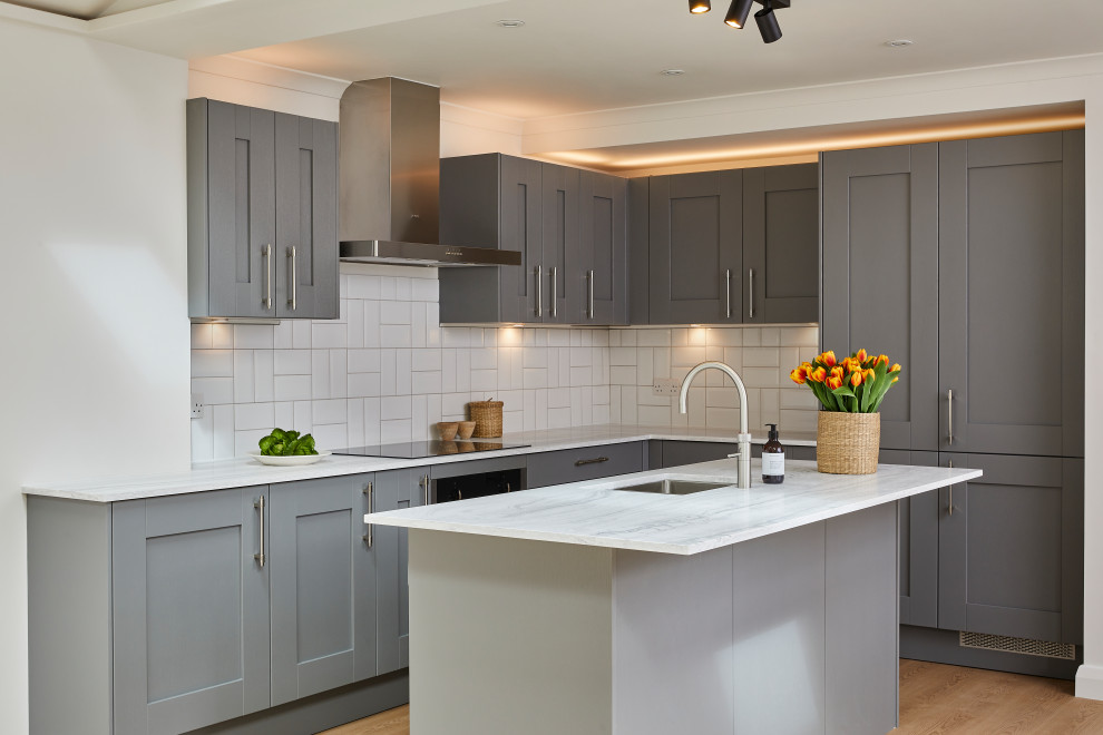 This is an example of a medium sized classic l-shaped open plan kitchen in London with a built-in sink, shaker cabinets, grey cabinets, quartz worktops, white splashback, ceramic splashback, stainless steel appliances, vinyl flooring, an island, beige floors and white worktops.