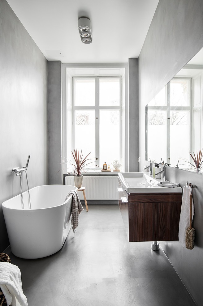 Scandinavian bathroom in Stockholm with flat-panel cabinets, dark wood cabinets, a freestanding tub, grey walls, a console sink and grey floor.