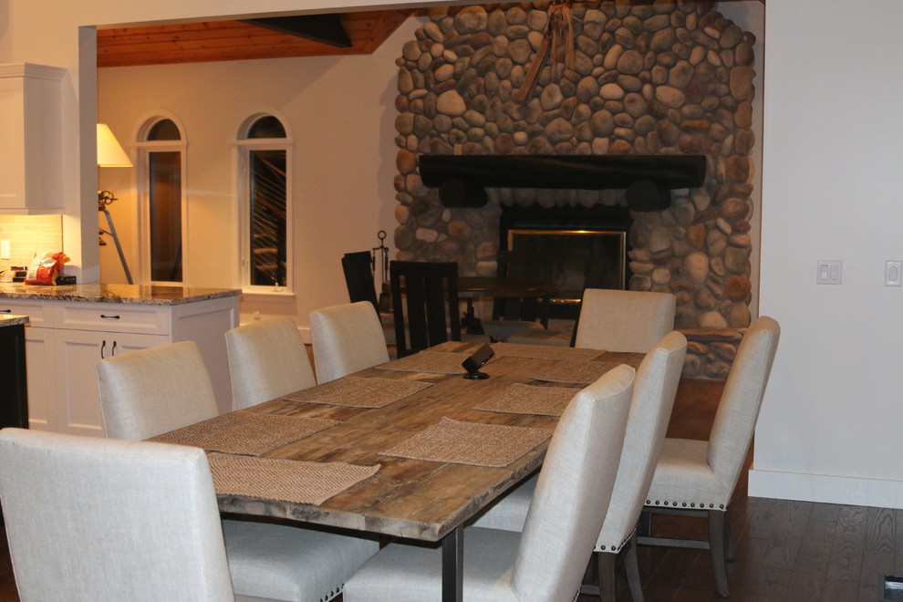 Exemple d'une grande salle à manger ouverte sur le salon industrielle avec un mur blanc, parquet foncé, une cheminée standard et un manteau de cheminée en pierre.