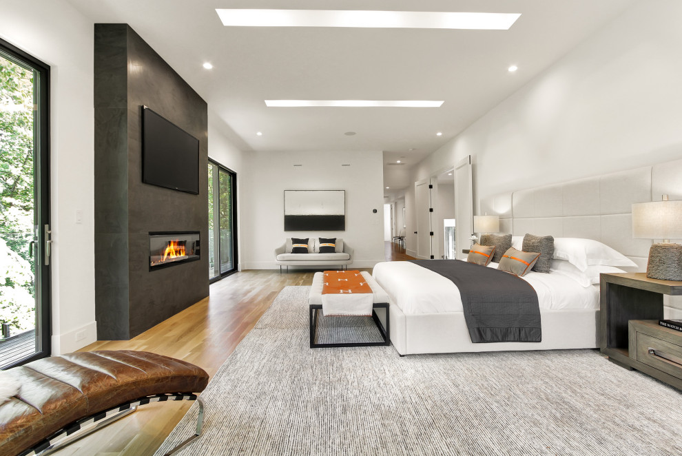 Large contemporary master bedroom in New York with white walls, light hardwood floors and a hanging fireplace.