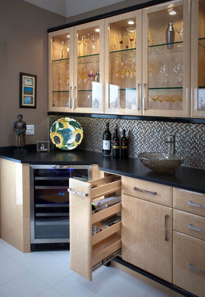 Mid-sized transitional l-shaped wet bar in Chicago with glass-front cabinets, light wood cabinets, solid surface benchtops, multi-coloured splashback, mosaic tile splashback and ceramic floors.