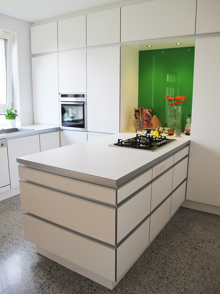 Design ideas for a mid-sized contemporary u-shaped kitchen in Berlin with a drop-in sink, flat-panel cabinets, white cabinets, green splashback, glass tile splashback, stainless steel appliances and a peninsula.