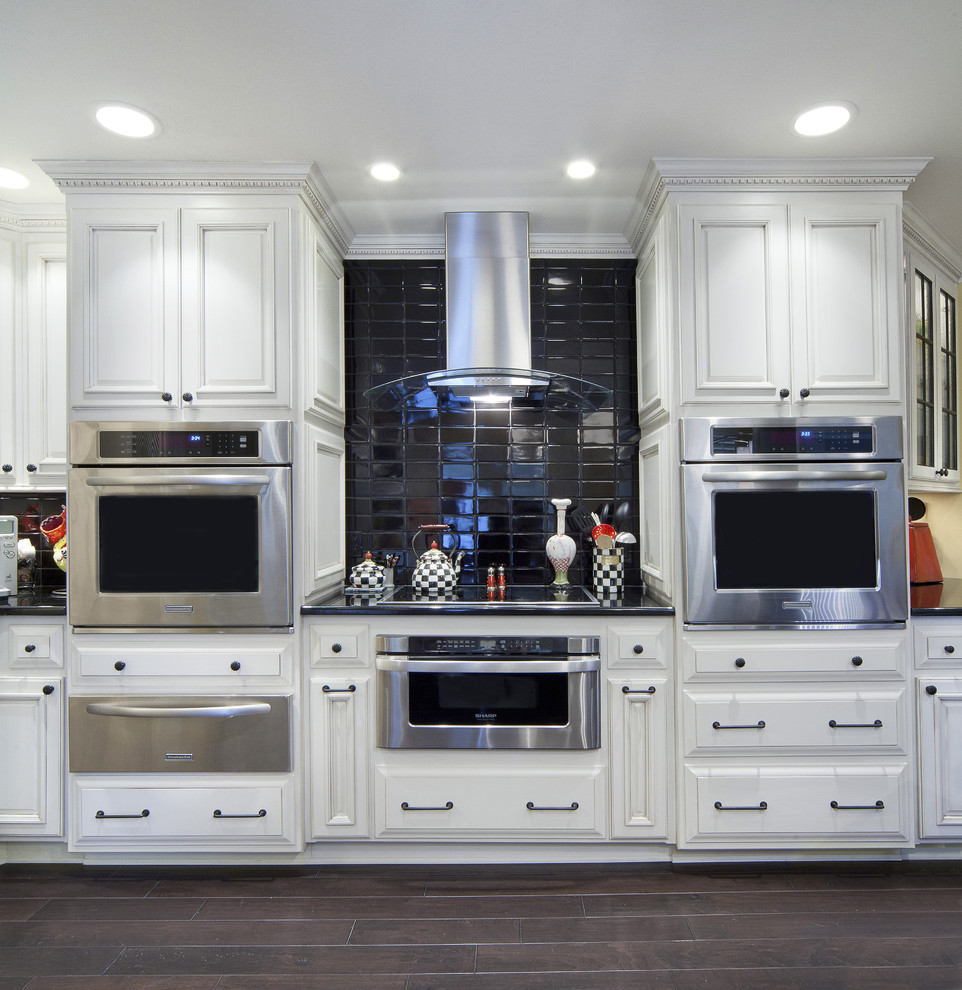 Inspiration for a large transitional kitchen in Little Rock with recessed-panel cabinets, white cabinets, quartzite benchtops, stainless steel appliances, dark hardwood floors, with island, a farmhouse sink, black splashback, ceramic splashback, brown floor and black benchtop.