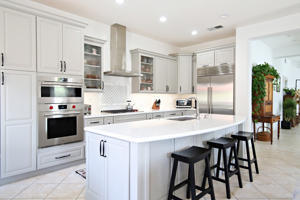 Mid-sized transitional l-shaped open plan kitchen in San Diego with an undermount sink, raised-panel cabinets, grey cabinets, quartz benchtops, white splashback, marble splashback, stainless steel appliances, travertine floors, with island, beige floor and white benchtop.