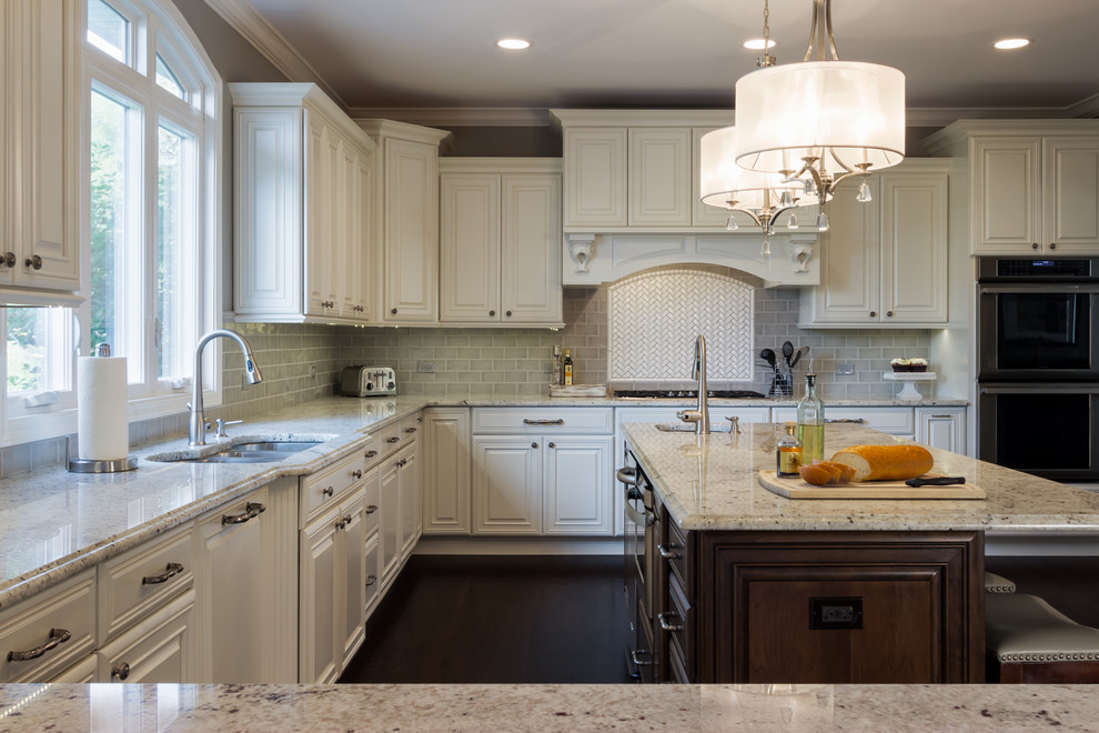 Example of a large transitional u-shaped dark wood floor kitchen design in Chicago with a double-bowl sink, raised-panel cabinets, white cabinets, granite countertops, gray backsplash, subway tile backsplash, stainless steel appliances and an island