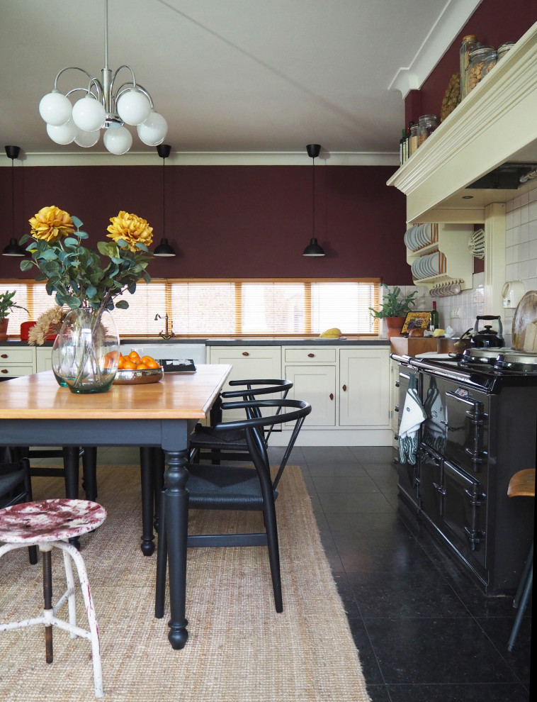 Photo of a mid-sized transitional single-wall eat-in kitchen in Amsterdam with a farmhouse sink, shaker cabinets, beige cabinets, window splashback, porcelain floors, no island, black floor and grey benchtop.