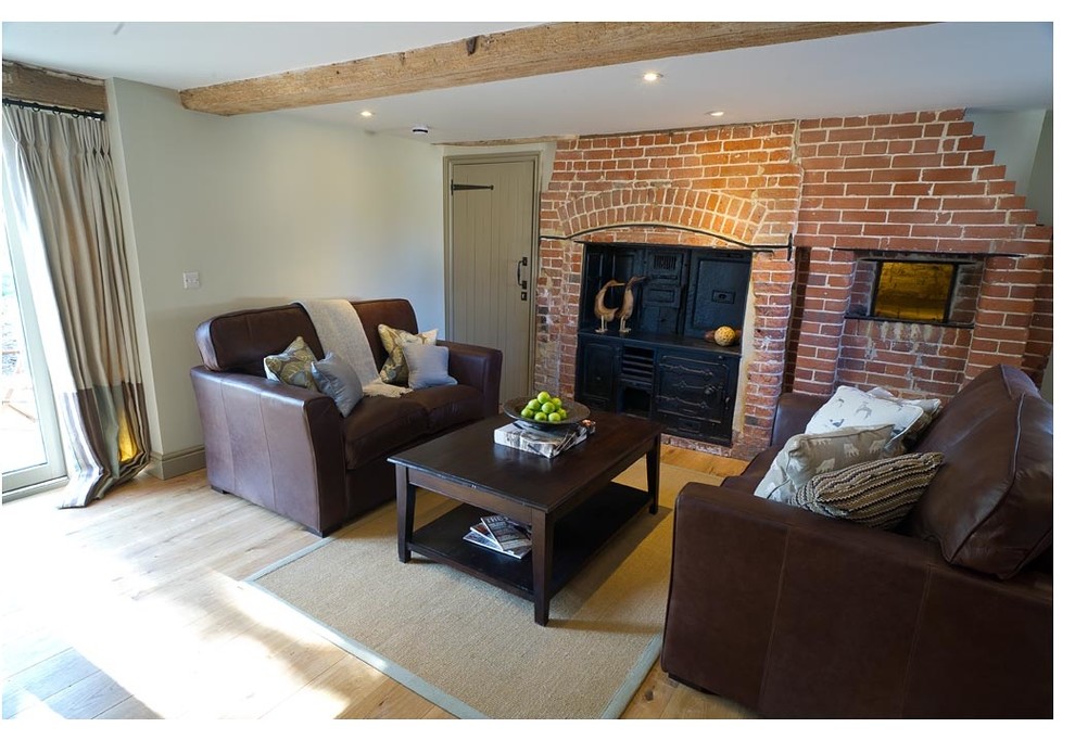 This is an example of a mid-sized country formal open concept living room in Hampshire with beige walls, light hardwood floors, a wood stove and a brick fireplace surround.