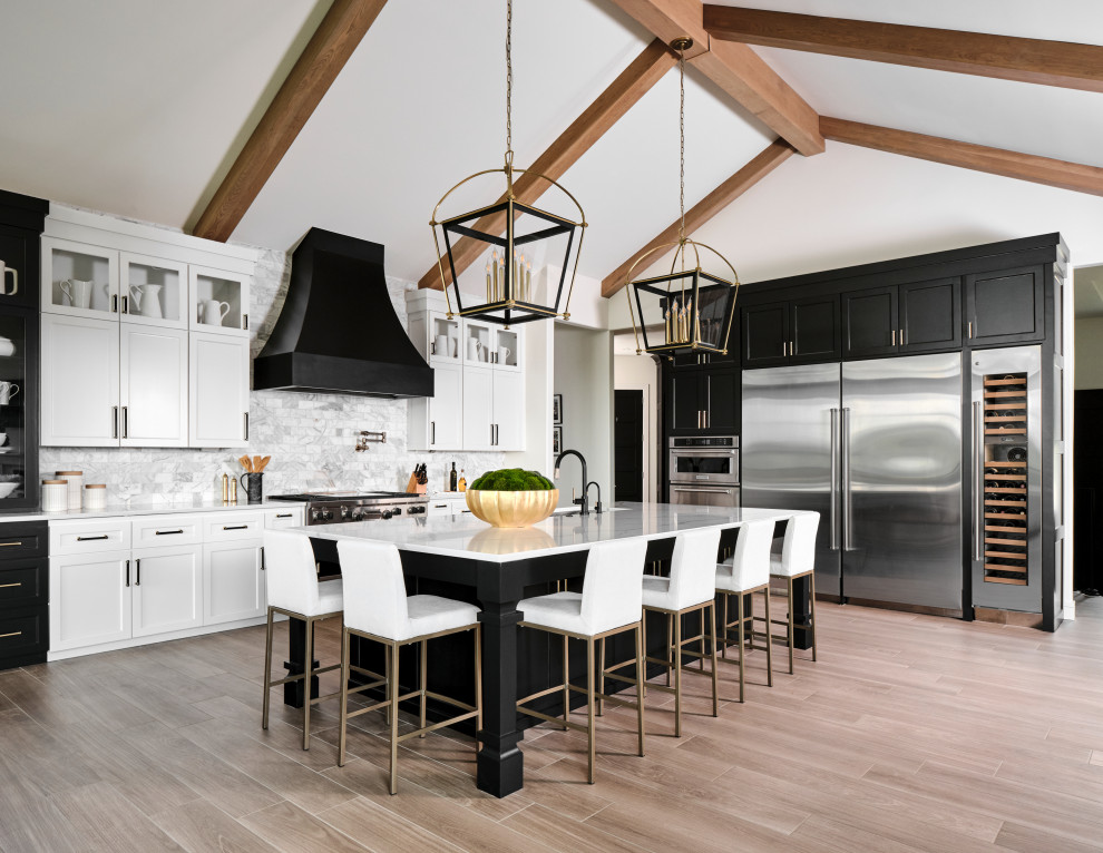 This is an example of an expansive country l-shaped open plan kitchen in Omaha with an undermount sink, shaker cabinets, black cabinets, quartz benchtops, grey splashback, marble splashback, stainless steel appliances, porcelain floors, with island, beige floor, white benchtop and vaulted.
