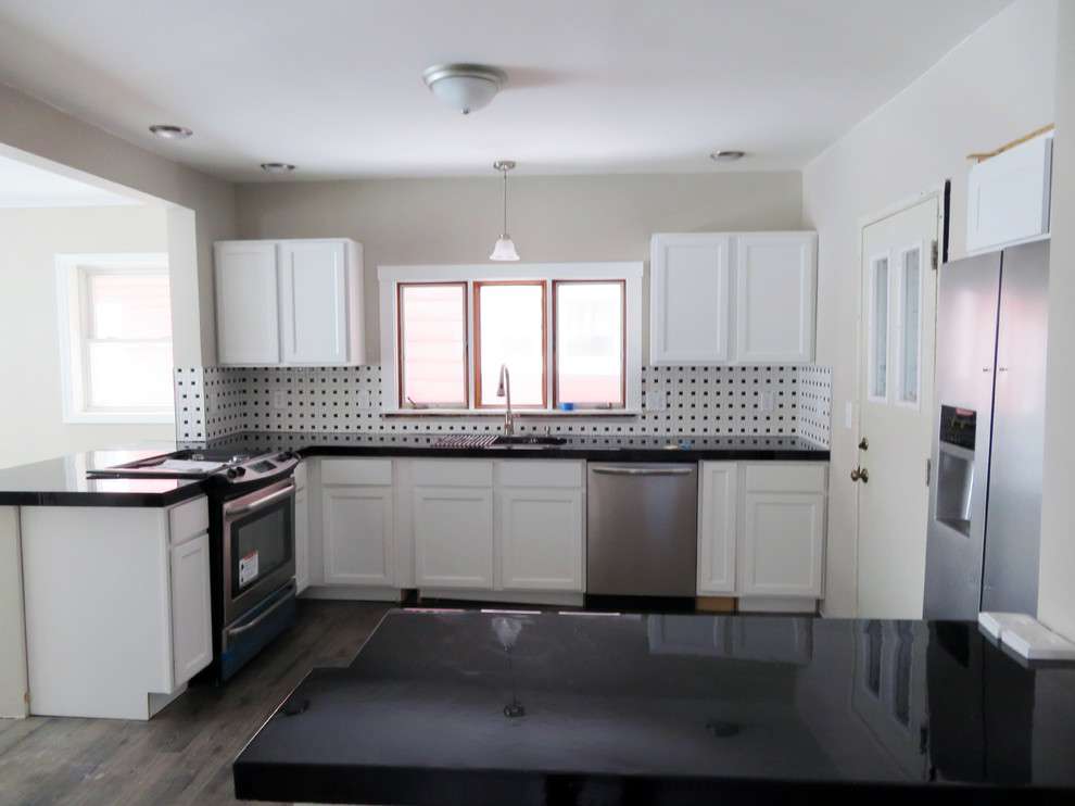 Example of a mid-sized transitional l-shaped vinyl floor and gray floor kitchen pantry design with recessed-panel cabinets, white cabinets, ceramic backsplash, stainless steel appliances, black countertops and concrete countertops