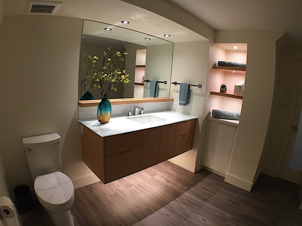 Photo of a mid-sized transitional 3/4 bathroom in Vancouver with flat-panel cabinets, medium wood cabinets, a double shower, a one-piece toilet, white tile, white walls, vinyl floors, an undermount sink, glass benchtops, grey floor and a sliding shower screen.
