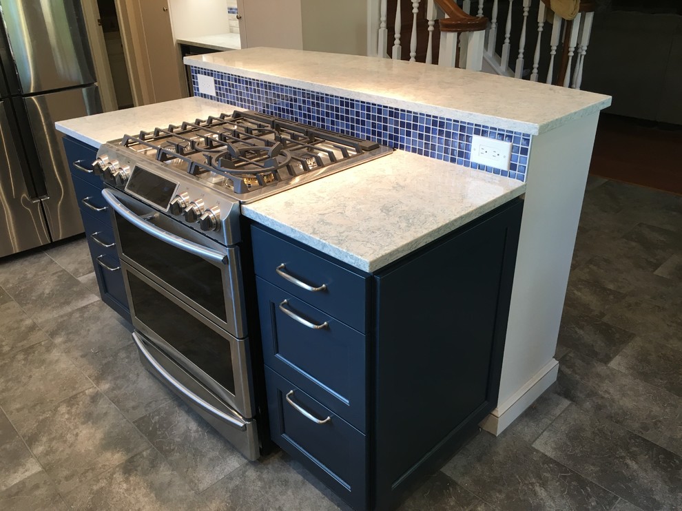 Large transitional l-shaped open plan kitchen in Houston with recessed-panel cabinets, blue cabinets, quartz benchtops, stainless steel appliances, porcelain floors, with island, grey floor, blue splashback and glass tile splashback.