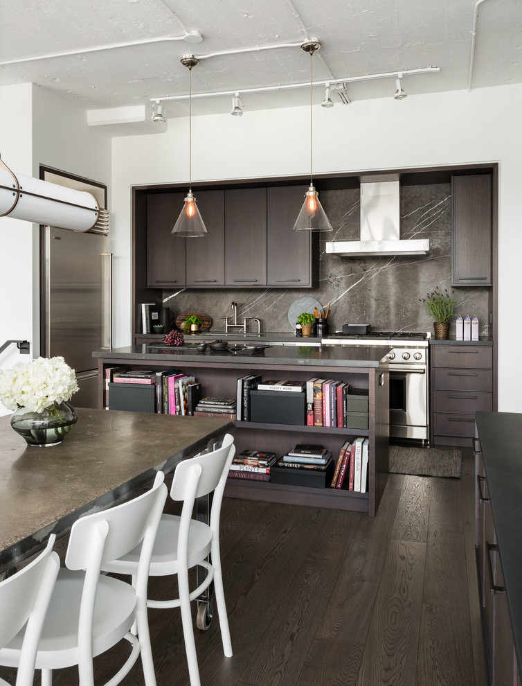 Mid-sized industrial l-shaped eat-in kitchen in Toronto with an undermount sink, flat-panel cabinets, dark wood cabinets, marble benchtops, stone slab splashback, stainless steel appliances, dark hardwood floors, with island, brown splashback and brown floor.