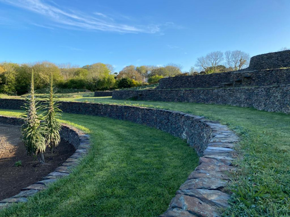 Photo of an expansive traditional sloped formal full sun garden for summer in Other with a retaining wall, natural stone paving and a stone fence.