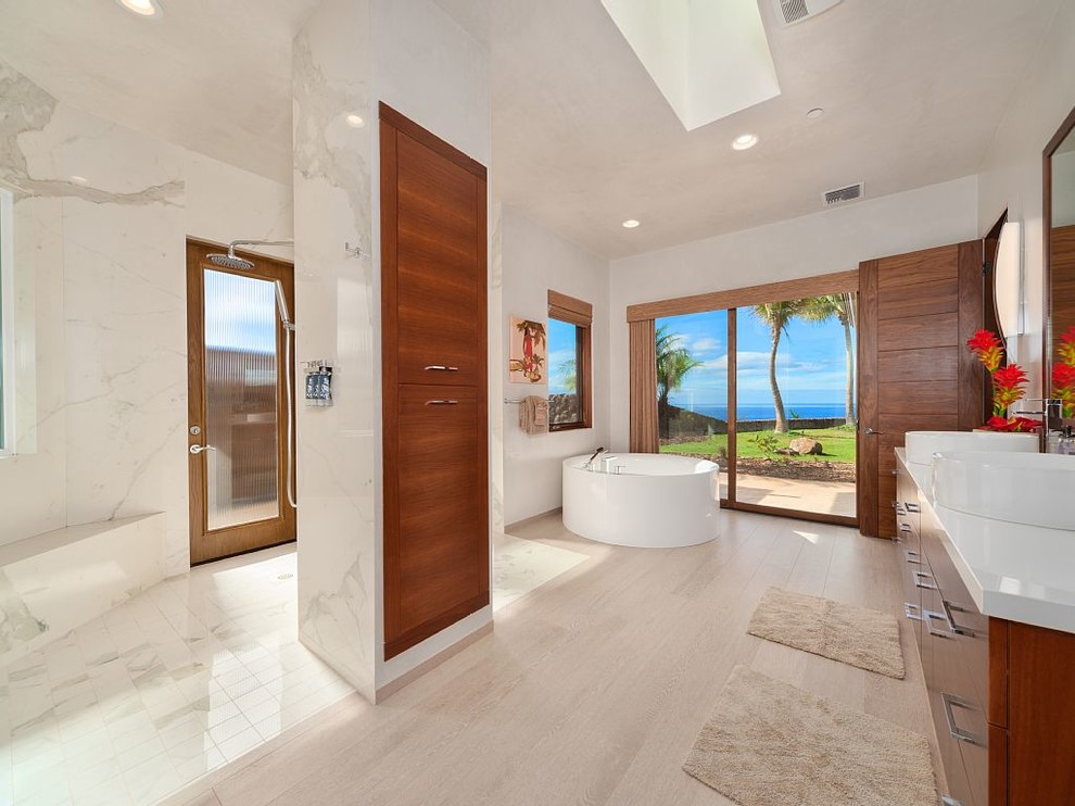 Photo of a large tropical master bathroom in Hawaii with flat-panel cabinets, dark wood cabinets, a freestanding tub, an open shower, white walls, white tile, stone slab, light hardwood floors, a vessel sink, engineered quartz benchtops, beige floor and an open shower.