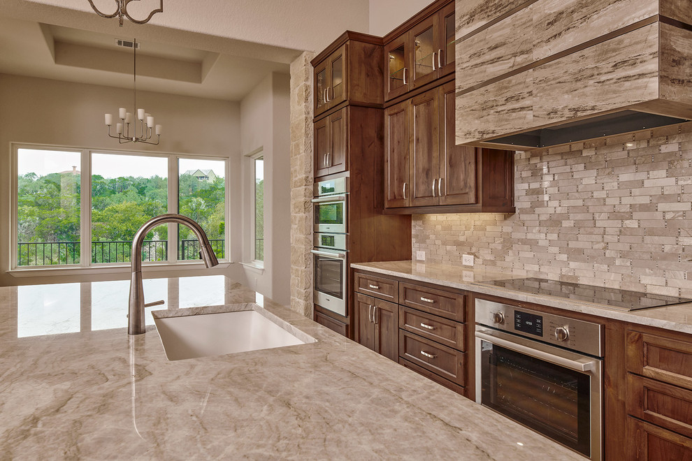 Design ideas for a mid-sized transitional eat-in kitchen in Austin with an undermount sink, recessed-panel cabinets, brown cabinets, wood benchtops, beige splashback, marble splashback, stainless steel appliances, marble floors, with island, beige floor and beige benchtop.
