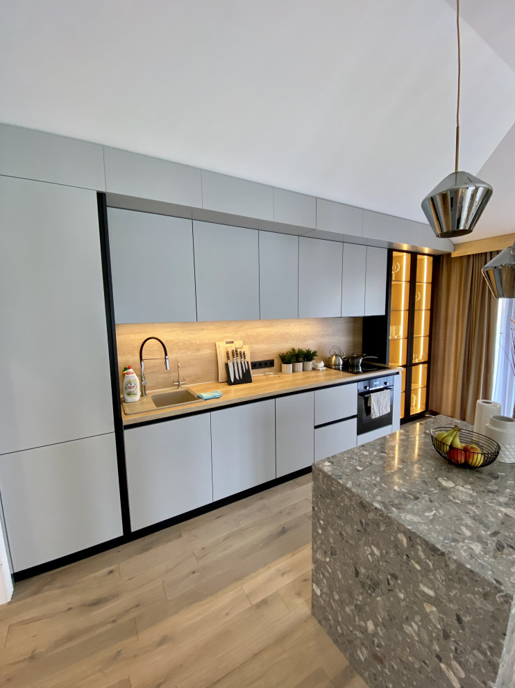 Exempel på ett stort modernt brun linjärt brunt kök med öppen planlösning, med en nedsänkt diskho, släta luckor, grå skåp, träbänkskiva, beige stänkskydd, stänkskydd i trä, svarta vitvaror, laminatgolv, en köksö och brunt golv