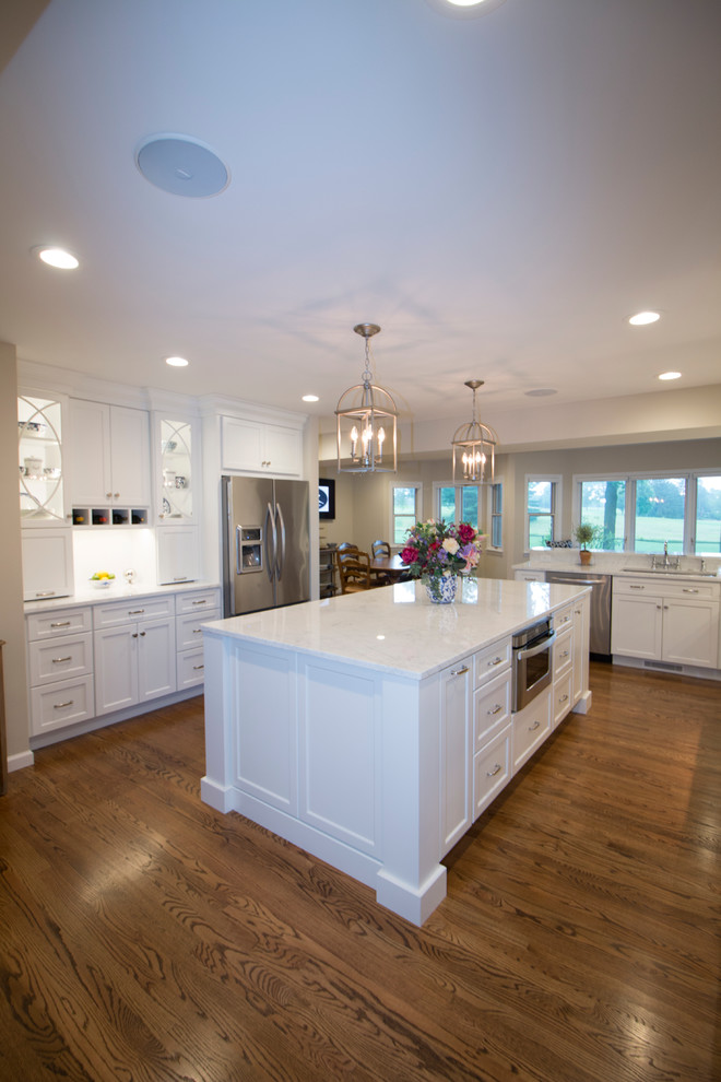 Open concept kitchen - huge transitional medium tone wood floor open concept kitchen idea with an undermount sink, shaker cabinets, white cabinets, marble countertops, white backsplash, ceramic backsplash, stainless steel appliances and two islands