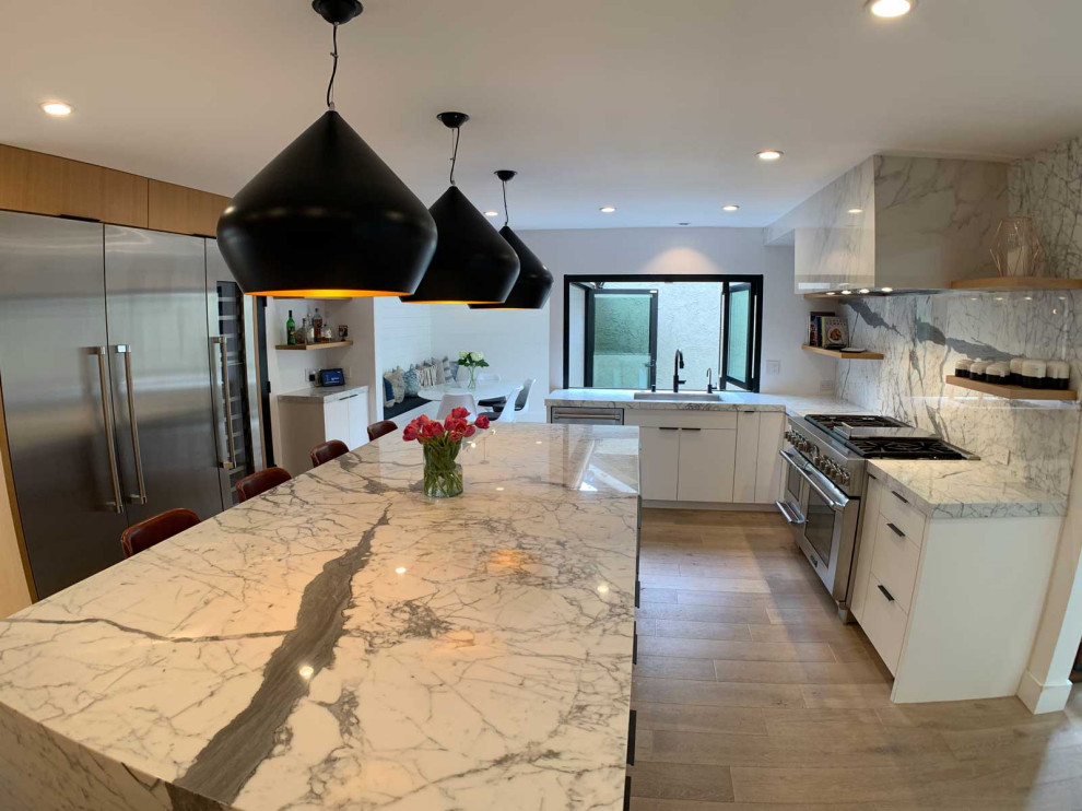 This is an example of a large l-shaped kitchen pantry in Orange County with a farmhouse sink, shaker cabinets, white cabinets, granite benchtops, white splashback, granite splashback, stainless steel appliances, light hardwood floors, with island, brown floor, white benchtop and vaulted.