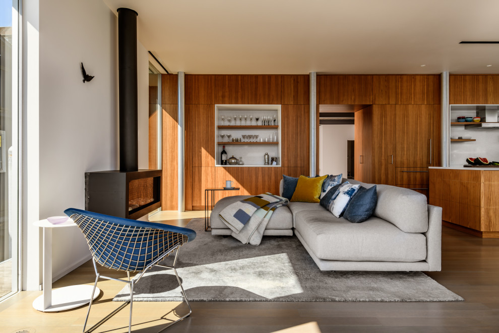 Diseño de salón abierto contemporáneo con paredes blancas, suelo de madera en tonos medios, chimeneas suspendidas y suelo marrón
