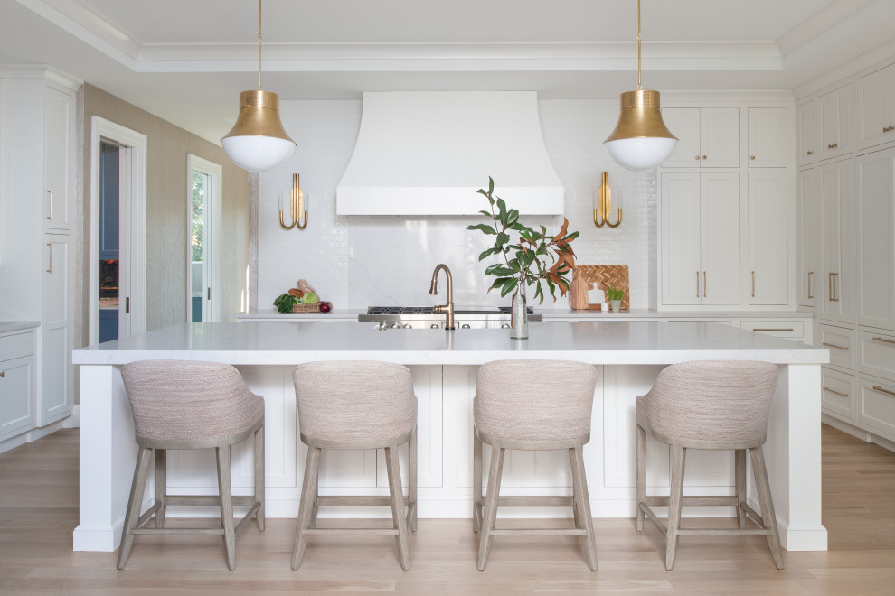 Design ideas for a transitional kitchen in DC Metro with a farmhouse sink, shaker cabinets, white cabinets, quartz benchtops, white splashback, subway tile splashback, panelled appliances, light hardwood floors, with island, white benchtop and recessed.