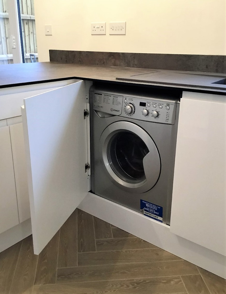 This is an example of a mid-sized modern u-shaped laundry room in Other with flat-panel cabinets, white cabinets, laminate benchtops, pink splashback, glass sheet splashback and grey benchtop.