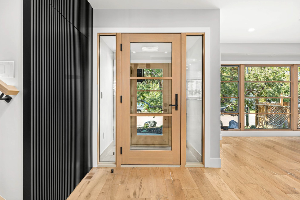 Diseño de entrada contemporánea con paredes blancas, suelo de madera clara, puerta simple y puerta de madera clara