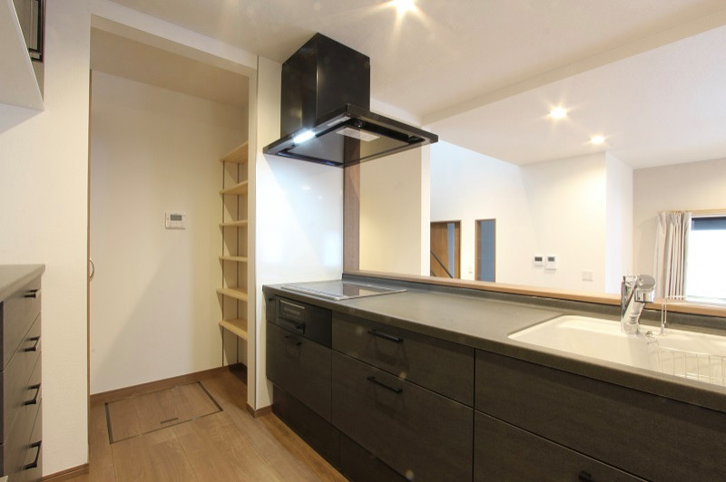 This is an example of a large country single-wall open plan kitchen in Other with an integrated sink, black cabinets, marble benchtops, white splashback, glass sheet splashback, stainless steel appliances, plywood floors, brown floor, black benchtop and wallpaper.
