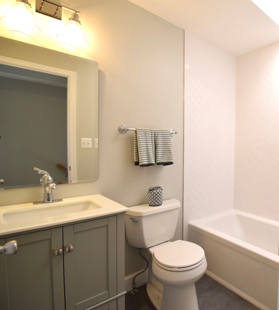 Photo of a mid-sized transitional kids bathroom in DC Metro with shaker cabinets, grey cabinets, an alcove tub, a shower/bathtub combo, a two-piece toilet, white tile, porcelain tile, grey walls, porcelain floors, a drop-in sink, solid surface benchtops, grey floor and white benchtops.