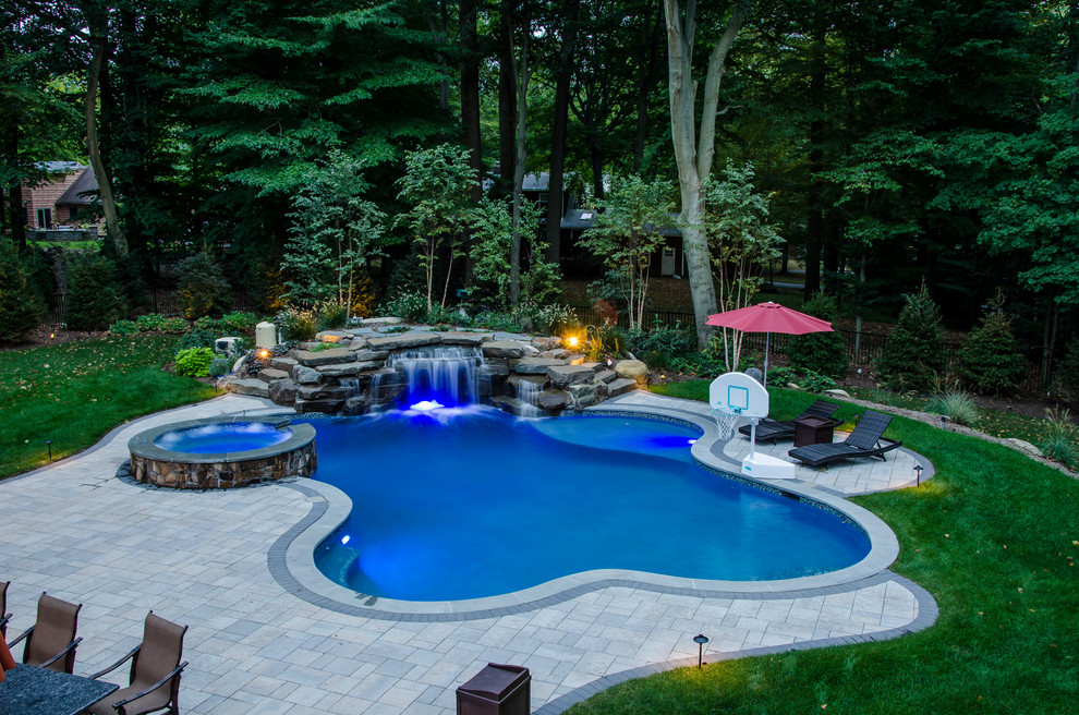 This is an example of a large transitional backyard custom-shaped natural pool in New York with a water feature and natural stone pavers.