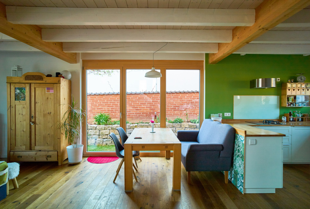 Cette image montre une salle à manger rustique avec un mur vert, un sol en bois brun et poutres apparentes.