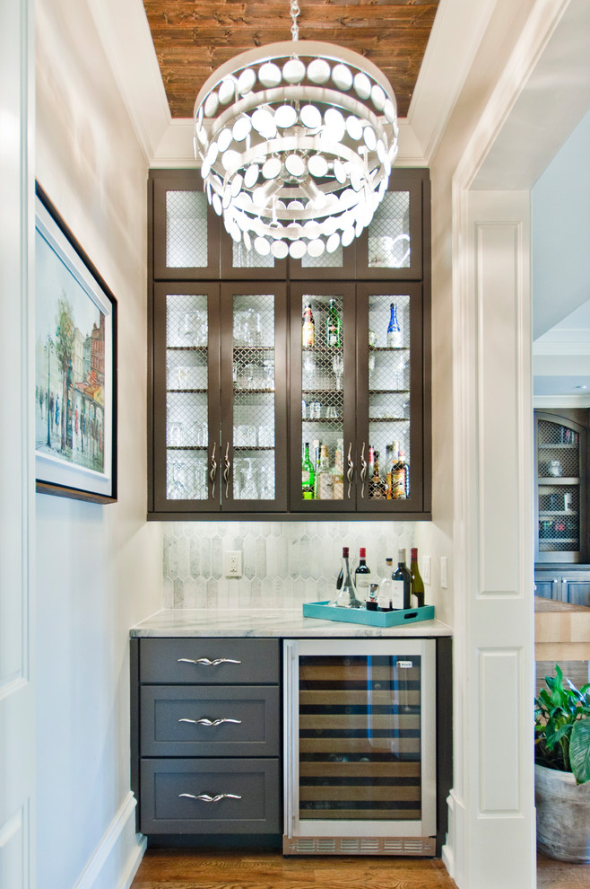 This is an example of a small transitional single-wall home bar in Nashville with shaker cabinets, granite benchtops, white splashback, marble splashback, medium hardwood floors, brown floor, no sink, multi-coloured benchtop and brown cabinets.