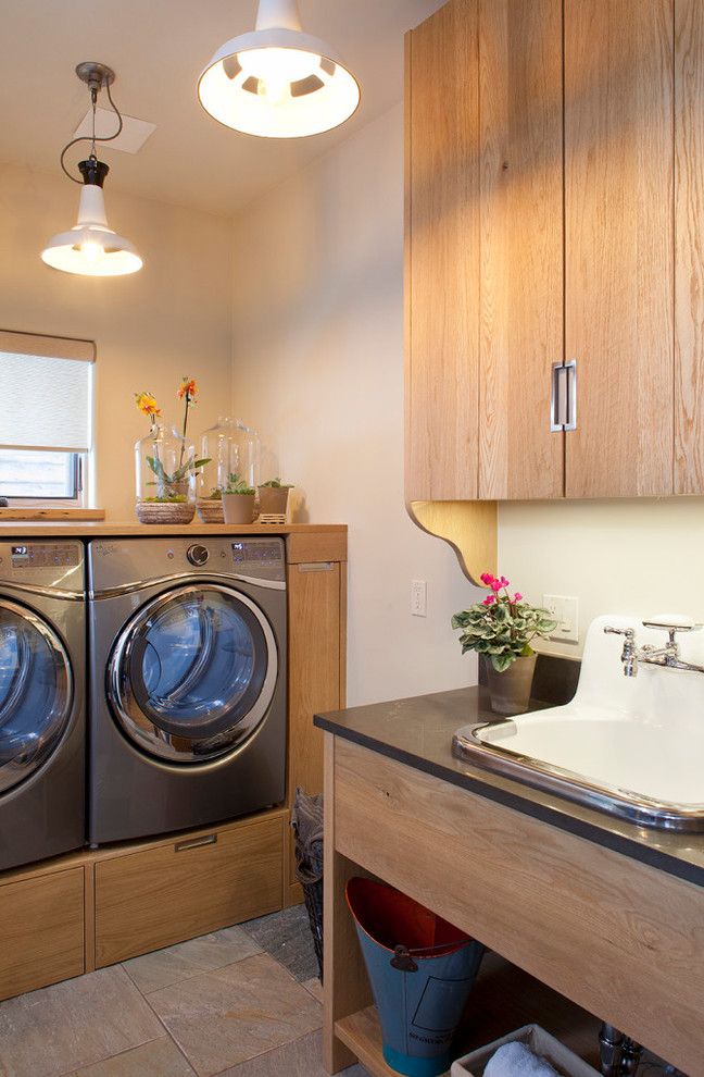 Design ideas for a transitional l-shaped dedicated laundry room in Denver with a drop-in sink, flat-panel cabinets, medium wood cabinets, white walls, a side-by-side washer and dryer, grey floor and grey benchtop.