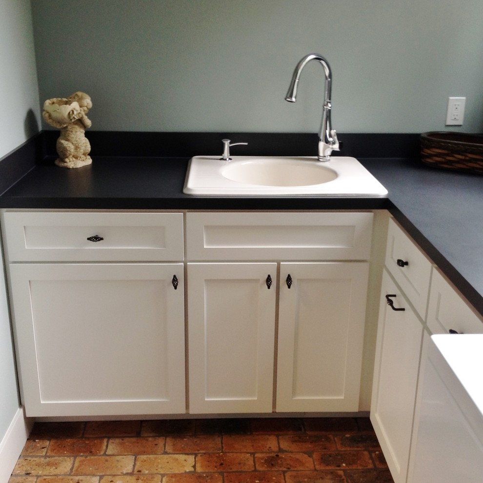 Inspiration for a traditional l-shaped laundry room in Seattle with a single-bowl sink, recessed-panel cabinets, white cabinets, grey walls and brick floors.