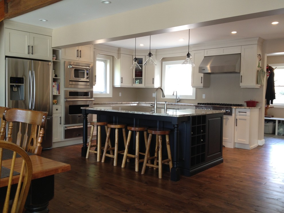 Inspiration for a mid-sized transitional l-shaped medium tone wood floor eat-in kitchen remodel in Toronto with a double-bowl sink, shaker cabinets, white cabinets, stainless steel appliances, an island and granite countertops