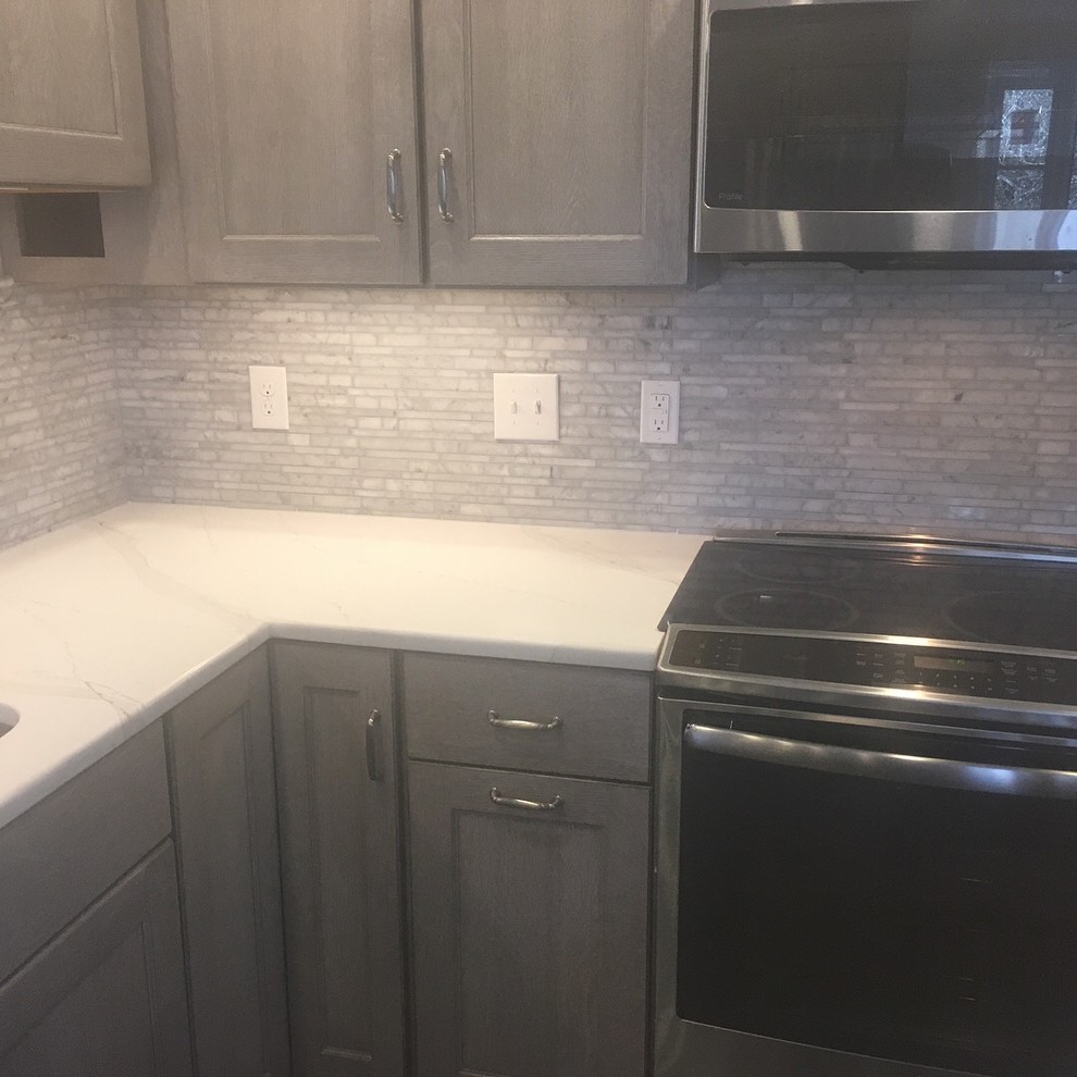 Mid-sized transitional u-shaped kitchen photo in Boston with an undermount sink, recessed-panel cabinets, gray cabinets, quartzite countertops, gray backsplash, stone tile backsplash, stainless steel appliances, no island and white countertops
