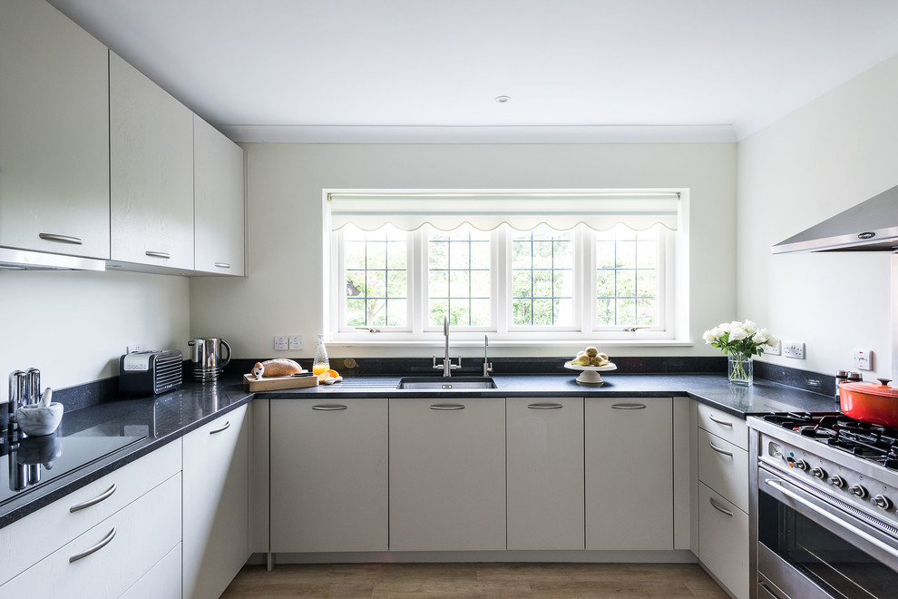 Inspiration for a mid-sized contemporary u-shaped open plan kitchen in Surrey with an undermount sink, flat-panel cabinets, grey cabinets, quartzite benchtops, black splashback, stainless steel appliances, laminate floors, no island, beige floor and black benchtop.