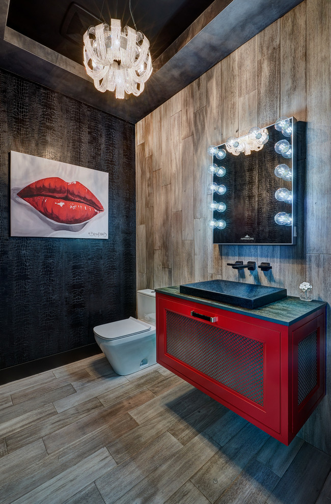 This is an example of a large industrial powder room in Sacramento with red cabinets, a one-piece toilet, black walls, light hardwood floors, a vessel sink, engineered quartz benchtops, grey benchtops, recessed-panel cabinets, brown tile and beige floor.